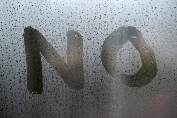 The English word "No" is written with a finger on the surface of the misted glass