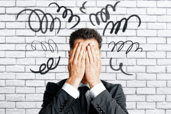 Worried businessman covering face on white brick
