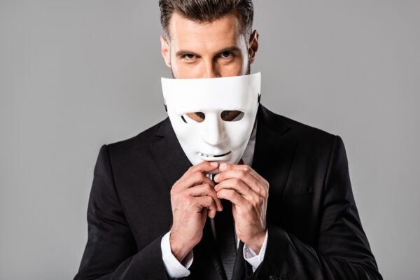 Businessman in black suit taking off white mask isolated on grey