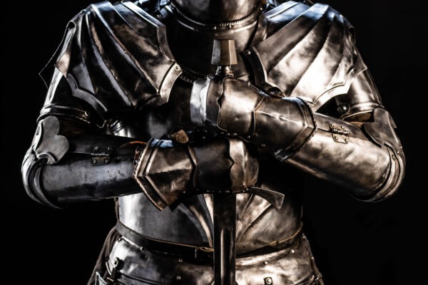 Cropped view of knight in armor holding sword isolated on black.