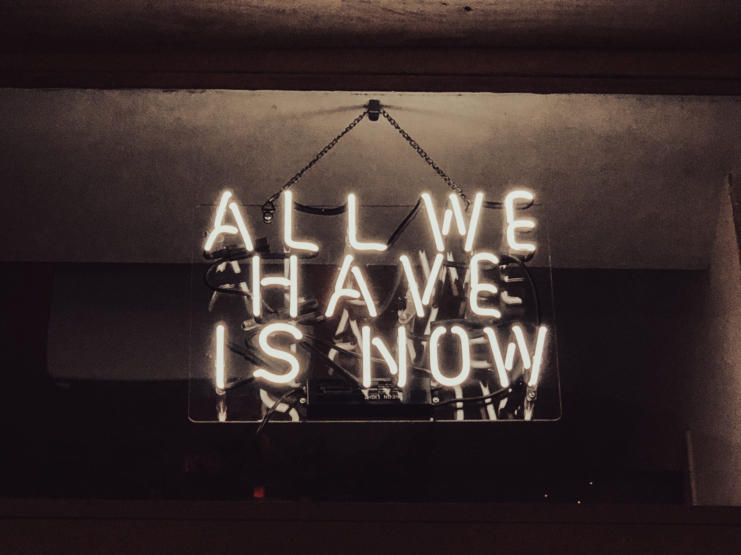 The quote "All We Have is Now" in neon lights.
