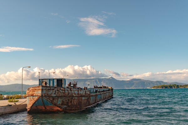 View of old rusty argosy near pier in Ionian sea. Beautiful landscape of Corfu island, mountains on background in sunny day.