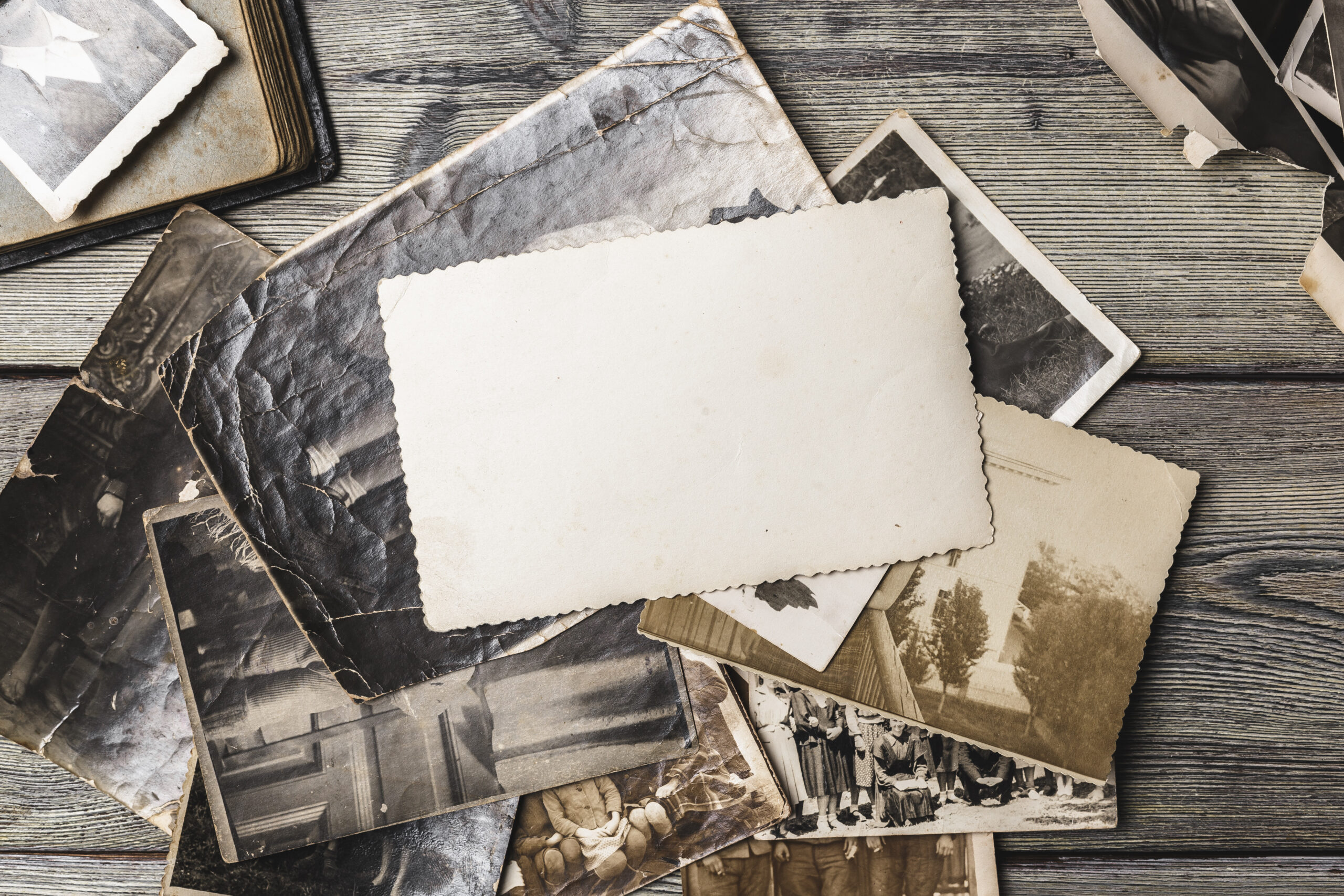 Scattered old photographs are on a wooden table with a blank card in the middle for notes.