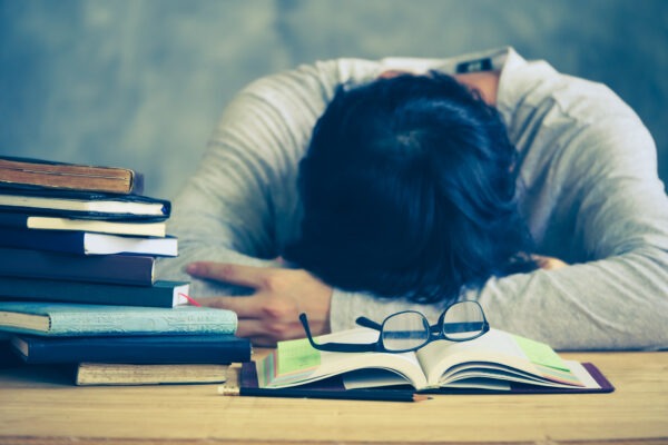 Tired young man sleeping with book stacks on the wooden table. Vintage tone
