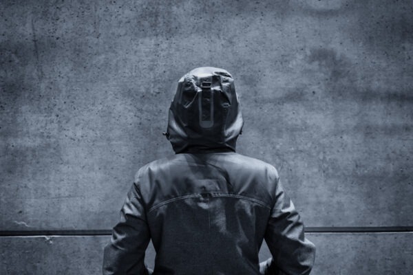 Unrecognizable hooded female person facing concrete wall as insurmountable obstacle, young adult woman in urban surrounding confronting problems and difficulties in life.