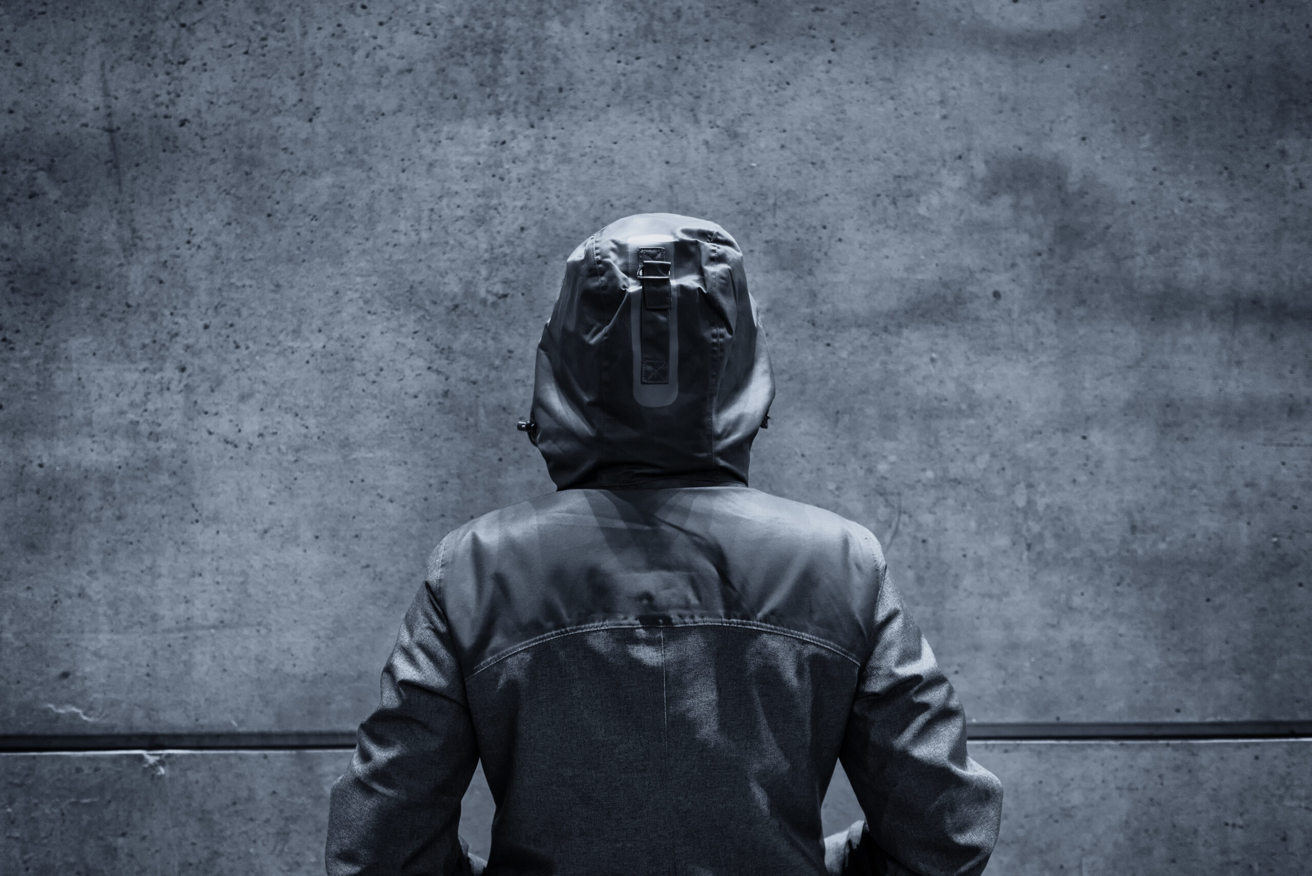 Unrecognizable hooded female person facing concrete wall as insurmountable obstacle, young adult woman in urban surrounding confronting problems and difficulties in life.