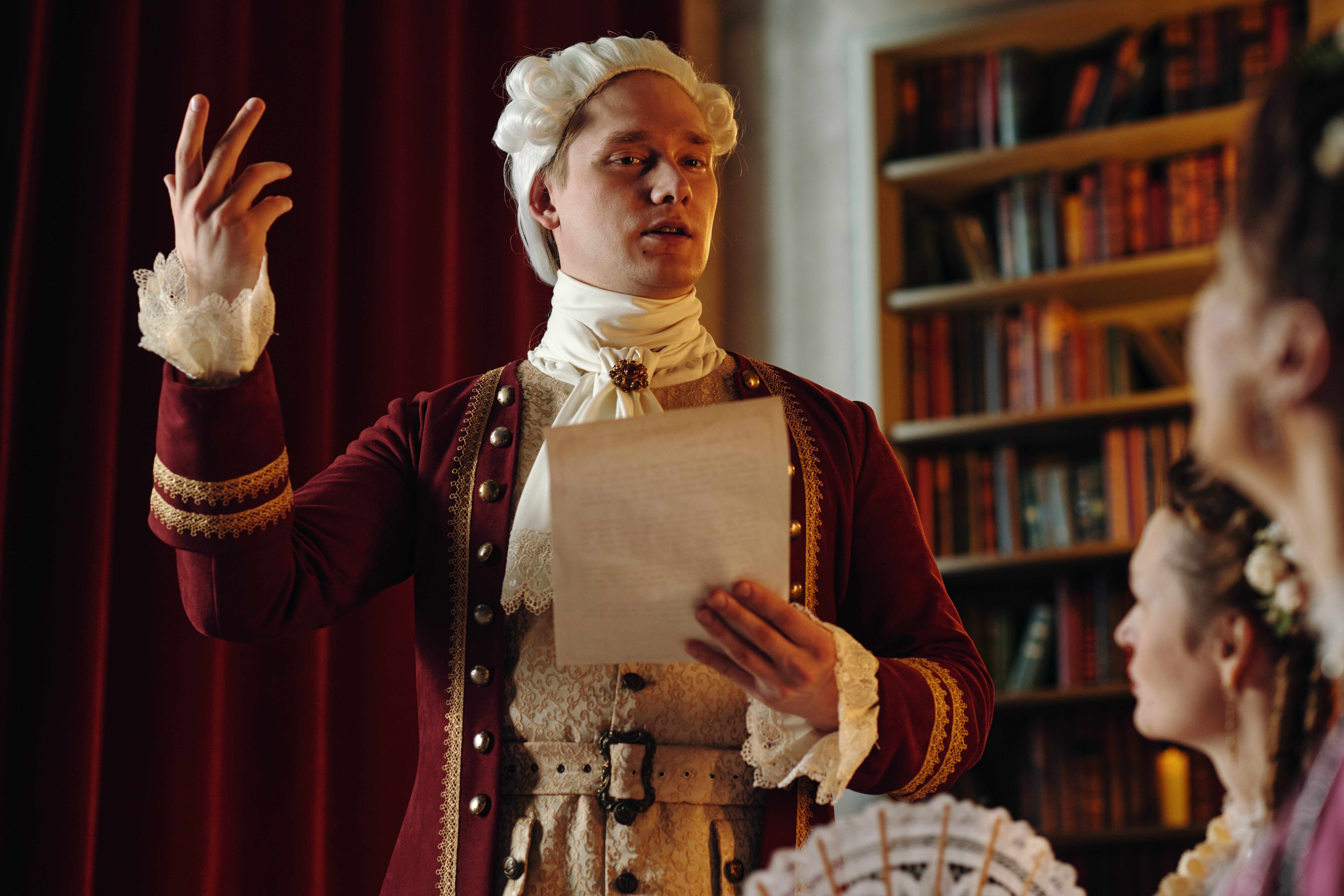 Young adult man wearing historical Baroque costume holding paper and gesturing while speaking to group of people