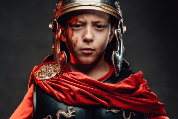 Kid dressed in dark armor with helmet and red cape.
