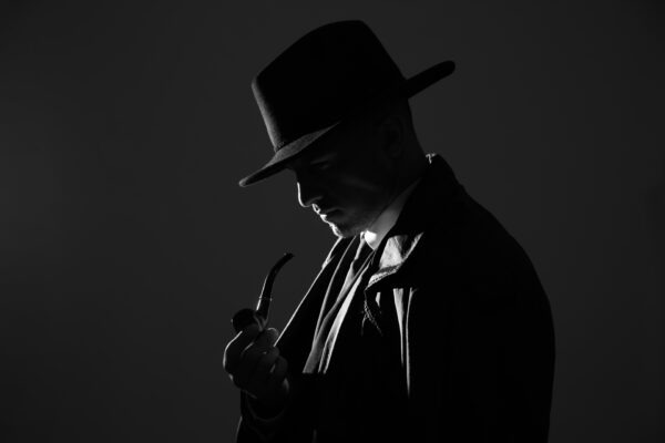 Old fashioned detective with smoking pipe on dark background, black and white effect