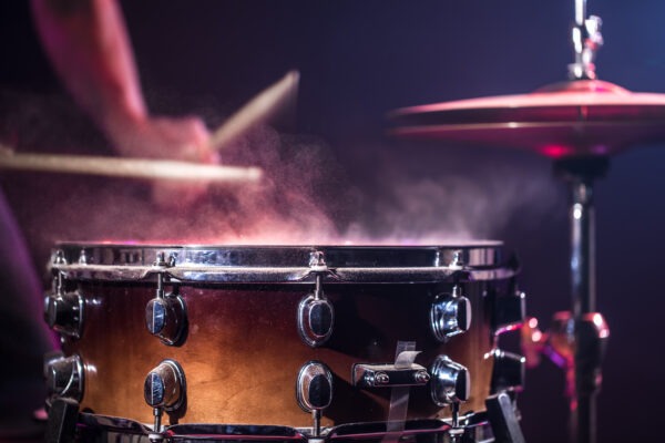 The drummer plays the drums. Beautiful blue and red background, with rays of light. Beautiful special effects smoke and lighting. The process of playing a musical instrument. The concept of music. Close-up photo.